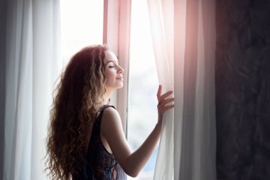 femme ouvrant les rideaux le matin au réveil